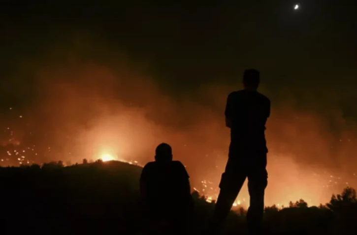 Deux personnes regardent des incendies près du village de Malona sur l'île touristique grecque de Rhodes, le 23 juillet 2023 ( AFP / SPYROS BAKALIS )