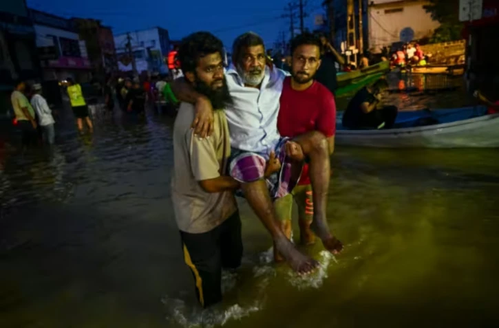 De jeunes hommes portent une personne âgée dans une rue inondée de Wellampitiya, dans les faubourgs de Colombo, la capitale du Sri Lanka, le 30 novembre 2025 ( AFP / Ishara S. KODIKARA )