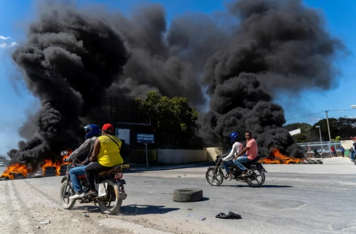 Des motos passent devant des pneus en feu après une manifestation de policiers consécutive à une attaque de gang sur un commissariat, à Port-au-Prince, le 26 janvier 2023