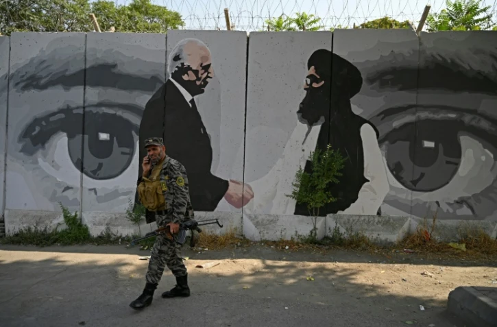 Un soldat passe devant une fresque murale dépeignant l'émissaire américain pour l'Afghanistan Zalmay Khalilzad et le co-fondateur des talibans Mullah Abdul Ghani Baradar le 31 juillet 2020 à Kaboul    