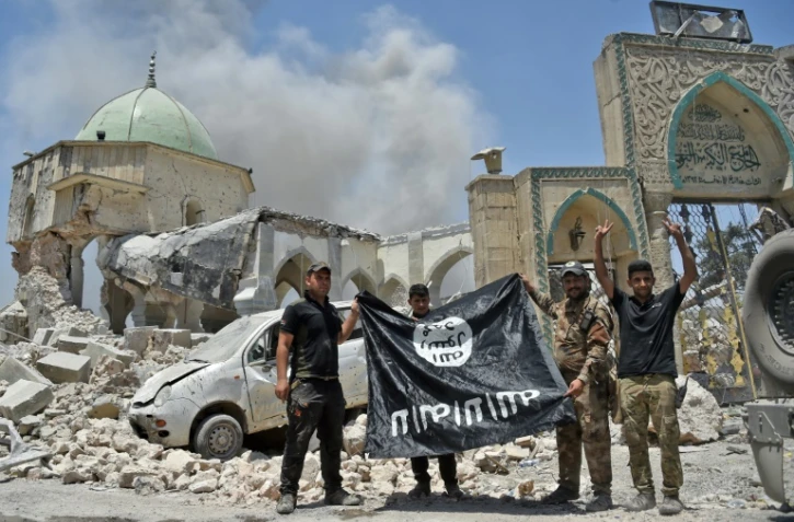 Un membre du Service du contre-terrorisme (CTS) irakien lève les bras en signe de victoire tandis que d'autres tiennent le drapeau de l'Etat islamique devant la mosquée al-Nouri de Mossoul, le 30 juin 2017