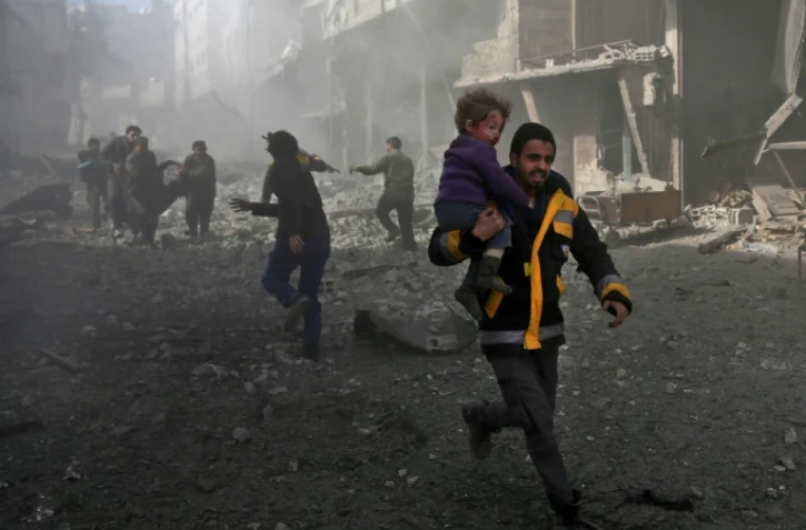 Un homme syrien court pour sauver un enfant après des bombardements du régime syrien contre la ville rebelle de Hammouriyé le 19 février 2018