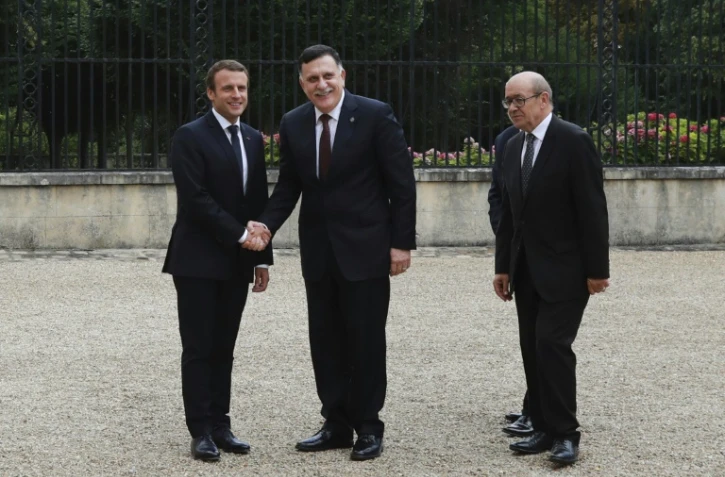 Le président Emmanuel Macron et le chef du gouvernement de Tripoli Fayyez al-Sarraj se serrent la main, accompagnés du ministre français des Affaires étrangères Jean-Yves Le Drian, à La Celle-Saint-Cloud, près de Paris, le 25 juillet 2017
