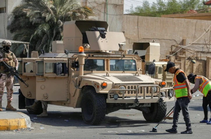 Des soldats montent la garde à l'entrée de la Zone verte pendant que des employés municipaux nettoient les rues après le retrait des partisans du leader chiite Moqtada Sadr, le 30 août 2022 à Bagdad, en Irak
