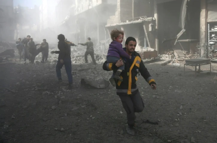 Un secouriste évacue un enfant tiré des gravats d'un immeuble, après une frappe aérienne, à Hammouriyé, dans la partie rebelle de la Ghouta orientale, le 19 février 2018