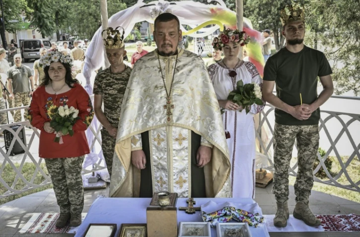 Des couples de militaires ukrainiens, Kristina et Vitali Orlich (à droite), ainsi que Kristina Liouta et Volodymyr Mikhalchouk (à gauche), pendant leur cérémonie de mariage dans la ville de Droujkivka, dans l'est de l'Ukraine, le 12 juin 2022