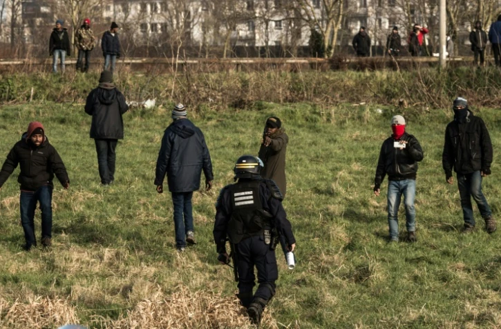 Un policier face à des migrants qui essaient de monter dans des camions sur l'A16 à Coquelles près de Calais le 21 janvier 2016