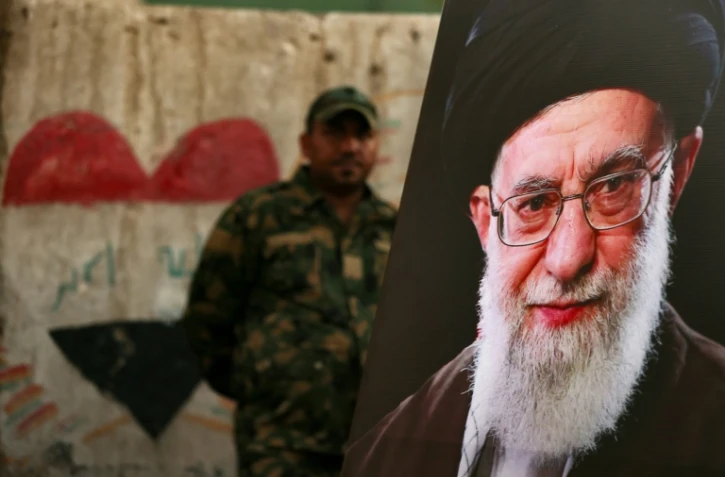 Un membre des Forces de mobilisation populaire irakiennes se tient derrière un portrait du guide suprême iranien défunt Ali Khamenei, à la veille de son cortège funère, au mausolée de l'imam Hussein à Karbala, en Irak, le 7 juillet 2026