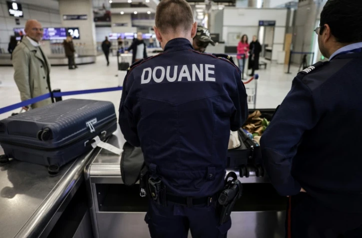 Des douaniers inspectent les bagages de passagers à l'aéroport de Roissy-Charles-de-Gaulle, au nord de Paris, le 21 mars 2025 