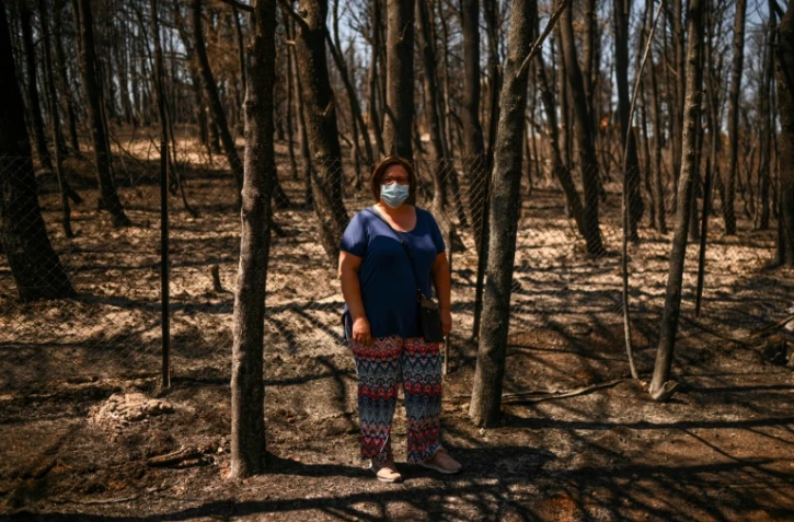 Eleni Haniosakis au milieu d'arbres calcinés, près de sa maison qui a brûlé dans les feux de forêt à Krioneri, au nord d'Athènes, le 13 août 2021 en Grèce