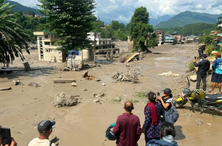 Des habitants observent des maisons partiellement submergées dans des eaux boueuses à la suite d'inondations soudaines survenues à Trishuli Bazar, dans le district de Nuwakot au Népal, le 26 août 2026.