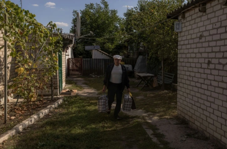 Serguiï, chargé de deux gros sacs, quitte sa maison pour être évacué par les membres de la Croix-Rouge ukrainienne, le 28 septembre 2023 à Bogouslavka, dans l'est de l'Ukraine