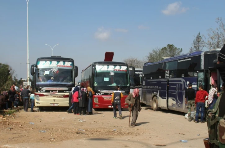 Un combattant rebelle devant des bus transportant des personnes évacuées la veille de localités syriennes loyalistes, le 15 avril 2017 à  Rachidine, une banlieue rebelle à l'ouest d'Alep 
