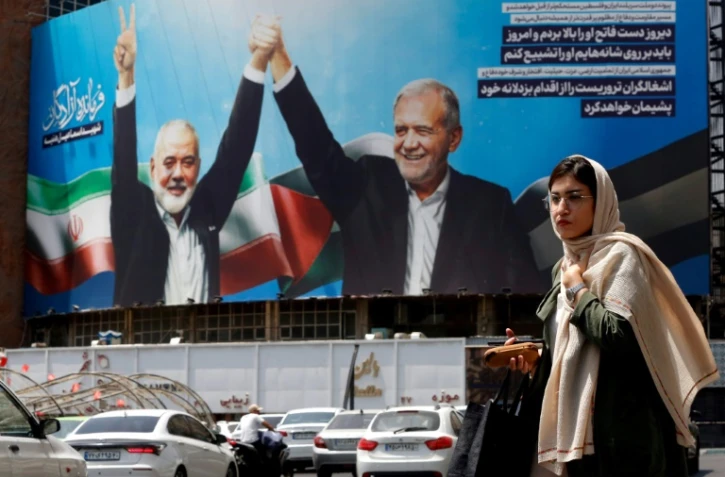 Une femme passe devant un panneau d'affichage représentant le président iranien Massoud Pezeshkian (à droite) et le chef du Hamas palestinien Ismaïl Haniyeh sur une place à Téhéran, le 8 août 2024