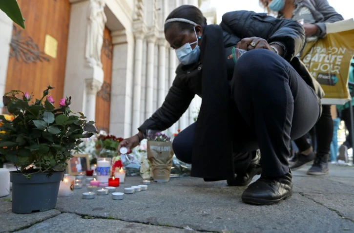 Une femme allume une bougie devant la basilique Notre-Dame à Nice lors d'un hommage aux victimes de l'attentat, le 30 octobre 2020 