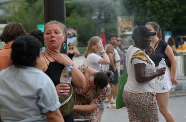 Des personnes se rafraîchissent en traversant un fin brouillard d'eau dans le centre de Paris le 21 juin 2025