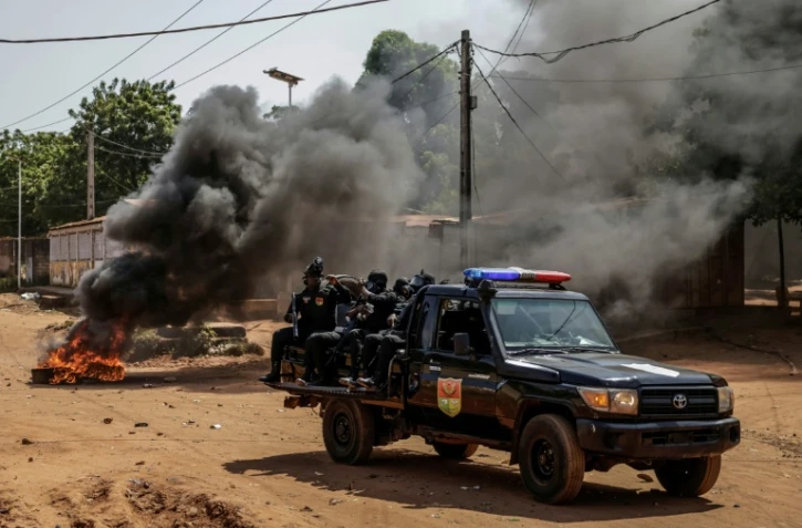 Un véhicule des forces de l'ordre passe à proximité  de pneus enflammés lors d'échauffourées dans la capitale bissau-guinéenne, le 29 novembre 2025