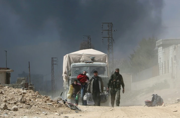 Un combattant des prorégime marche au côté de civils sortant de la localité de Hammouriyé dans l'enclave rebelle de la Ghouta orientale, cible d'une offensive du régime syrien, le 16 mars 2018 
