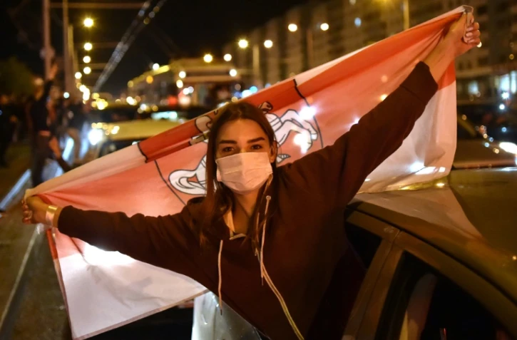 Une femme masquée portant l'ancien drapeau du Bélarus lors d'une manifestation d'opposition à Minsk, le 13 août 2020