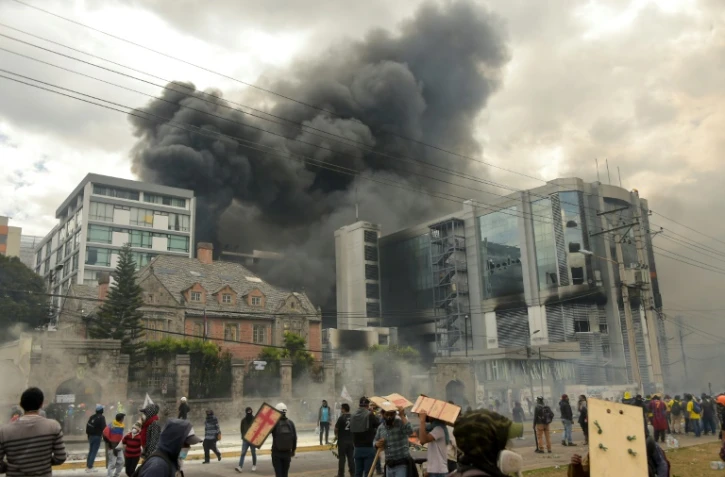 Des manifestants encagoulés mettent le feu au bureau de l'Inspection générale des finances, dans le nord de Quito, le 12 octobre 2019