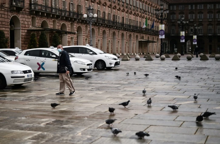 Un homme marche devant des taxis alignés sur la Piazza Castello à Turin, le 26 octobre 2020