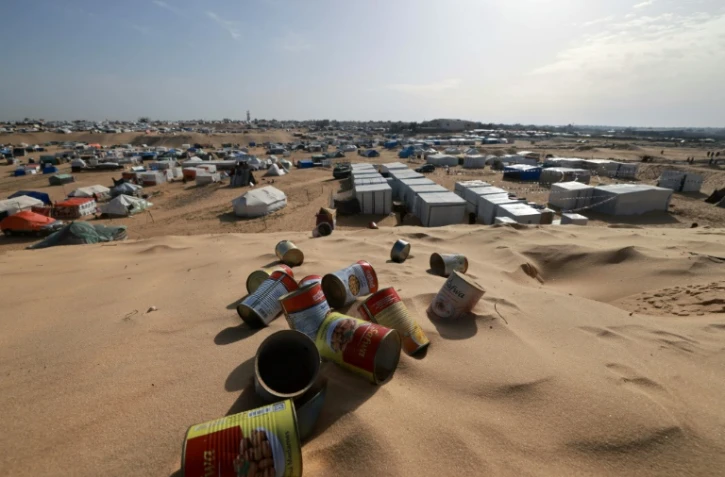 Des boîtes de conserve vides jonchent une dune de sable surplombant un camp de personnes déplacées à Rafah, dans le sud de la bande de Gaza, le 17 mars 2024