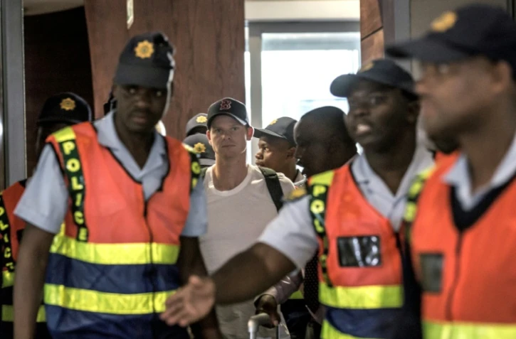 L'ex-capitaine de l'équipe nationale australienne de cricket Steve Smith (centre) quitte l'aéroport de Johannesburg, suite au scandale de la balle trafiquée qui a ébranlé le monde du cricket et l'Australie.