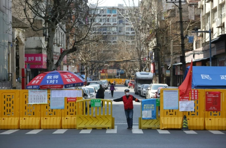 Un homme devant une barrière empêchant l'enrée dans un quartier confiné de Wuhan, le 15 mars 2020 pendant l'épidémie du nouveau coronavirus