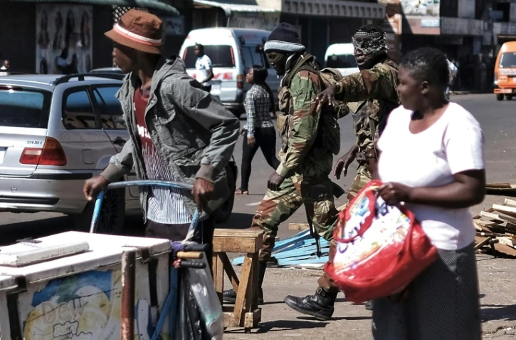 Deux soldats zimbabwéens cagoulés crient des ordres à des vendeurs de rue et des changeurs de billets, lors d'une patrouille dans les rues de Harare, le 2 août 2018