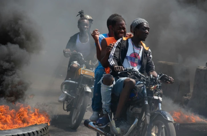 Des hommes à moto passent entre des pneus en feu lors d'une manifestation après l'annonce de la démission du Premier ministre Ariel Henry, à Port-au-Prince en Haïti, le 12 mares 2024