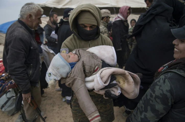 Un membre des Forces démocratiques syriennes (FDS) porte dans ses bras un enfant qui a fui avec sa famille le groupe Etat islamique à Baghouz, le 14 février 2019