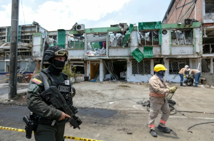 Un membre du Groupe des opérations spéciales de la police nationale colombienne monte la garde tandis que des agents de nettoyage déblayent les débris du site d'une explosion à la bombe survenue la veille à Cali, en Colombie, le 22 août 2025