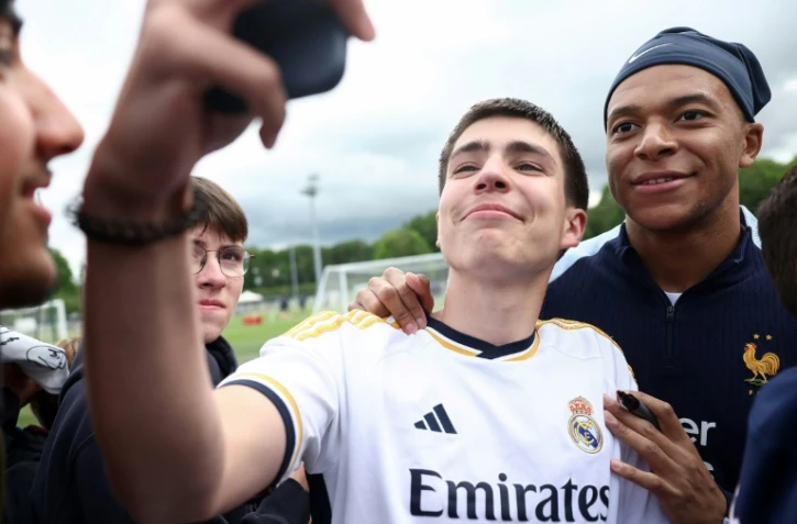 L'attaquant français Kylian Mbappé prend un selfie avec un fan portant un maillot du Real Madrid, le 30 mai 2024 à Clairefontaine-en-Yvelines