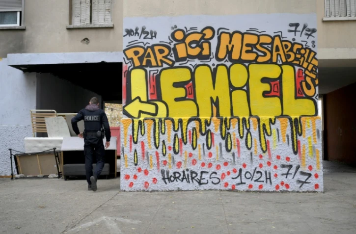 Un policier à côté d'un graffiti indiquant "Par ici mes abeilles, vous trouverez du miel ouvert 10/2h 7j/7" ,dans un point de dealer connu dans les quartiers nord de Marseille, le 1er décembre 2023