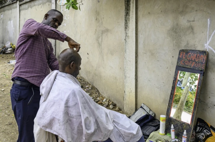 Papy Kalume, un coiffeur de rue, coupe les cheveux d'un client sur le trottoir Ă Kinshasa, le 17 octobre 2024 en RDC