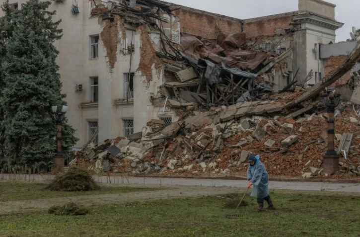 Un employé municipal ramasse de l'herbe coupée près d'un bâtiment administratif en partie détruit par une frappe russe, le 30 octobre 2026 à Kherson, dans le sud de l'Ukraine 
