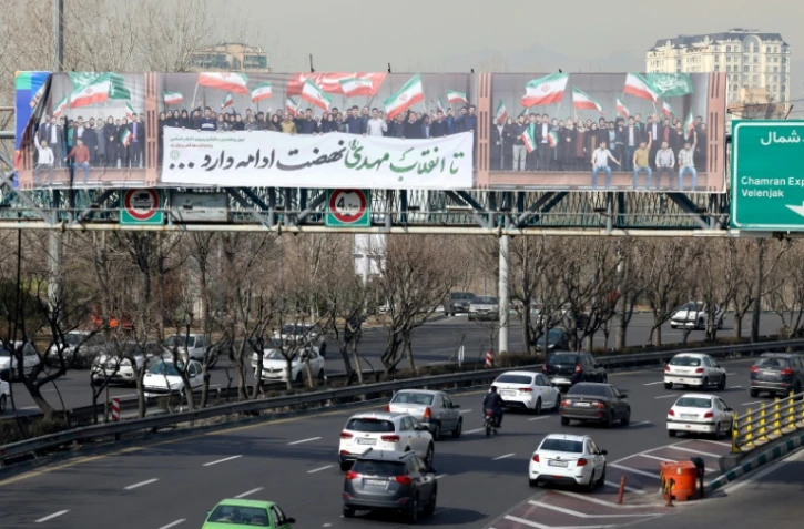 La passerelle piétonne d'une autoroute sur laquelle est déployée une immense banderole montrant des personnes agitant le drapeau iranien, à Téhéran, le 18 février 2026