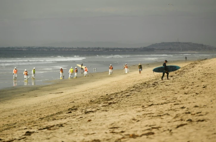 Un surfeur regagne la plage de Huntington Beach, en Californie, tandis que des équipes de nettoyage s'affairent à nettoyer l'impact de la marée noire, le 4 octobre 2021