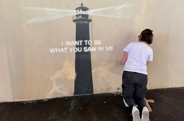 Agnès Perrone, peintre en décor du patrimoine, répare une œuvre d'art de l'artiste de rue Banksy représentant un phare sur la façade d'un bâtiment, après qu'elle a été vandalisée pendant la nuit à Marseille, le 1er juin 2025