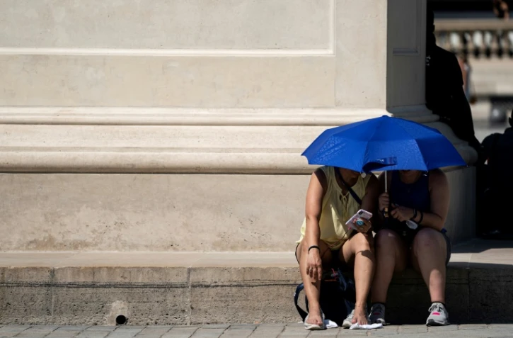 Des personnes se protègent du soleil près de la Pyramide du Louvre, à Paris le 26 juin 2019