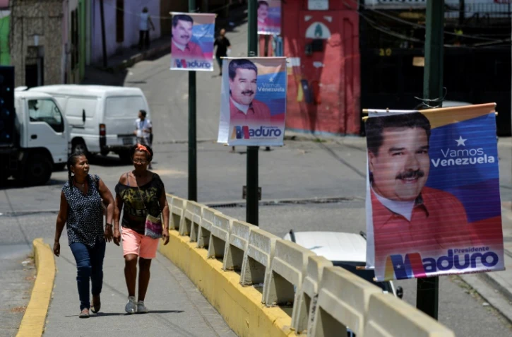 Des femmes marchent près d'une affiche de campagne du président vénézuélien Nicolas Maduro, dans les rues de Caracas, le 11 mai 2018