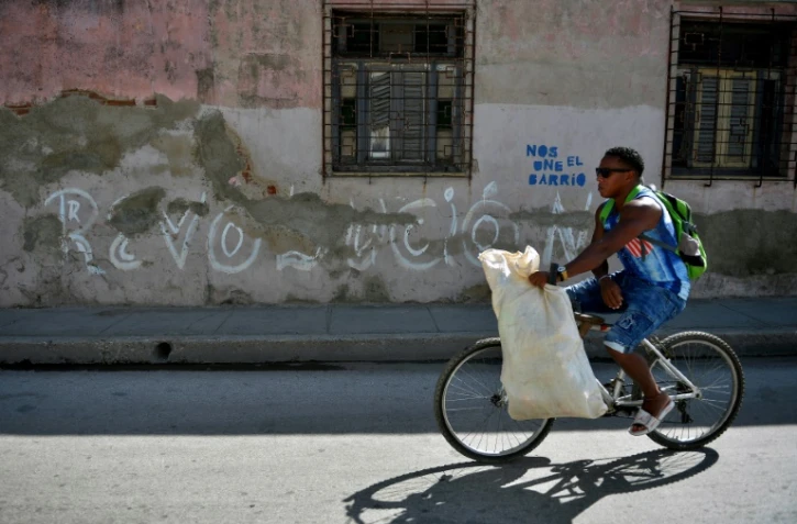 Un homme passe en vélo devant un graffiti "Revolucion" à Santiago de Cuba, le 31 décembre 2018