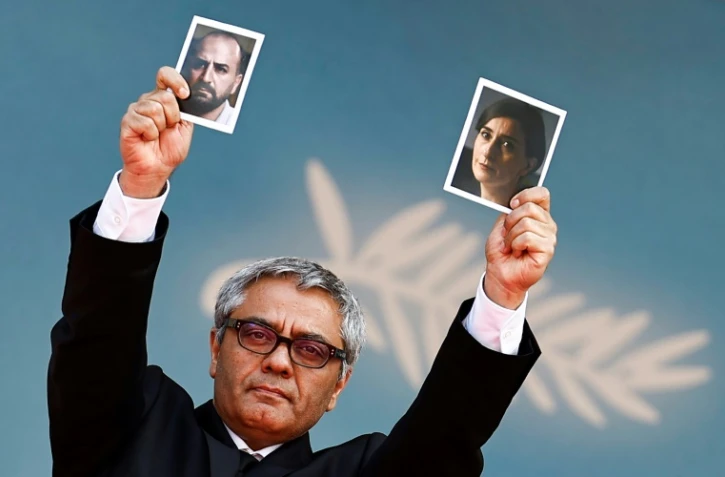Le réalisateur iranien Mohammad Rasoulof brandit les photos de l'acteur iranien Missagh Zareh, à gauche, et de l'actrice iranienne Soheila Golestani, à droite, le 24 mai 2024, au festival de Cannes, dans les Alpes-Maritimes