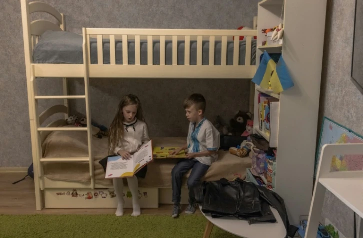 Nadiya Mikhailyuk lit un livre à côté de son frère Makar avant la rentrée des classes, le 1er septembre 2023 à Irpin, près de Kiev, en Ukraine