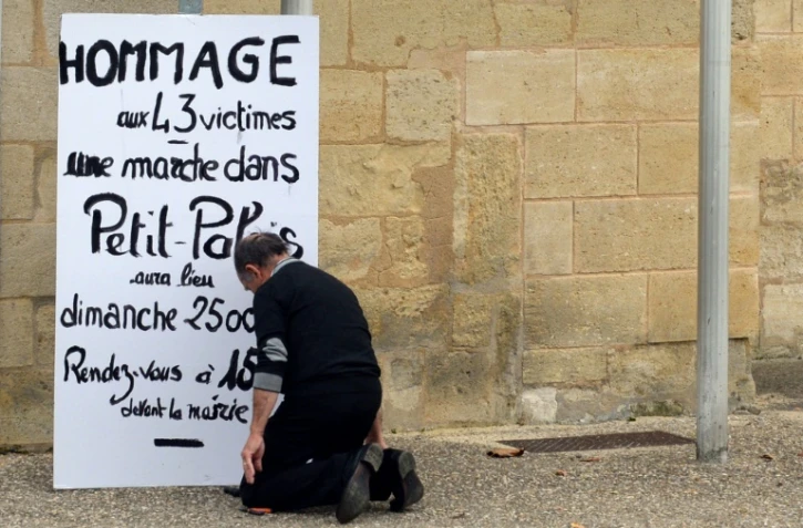 Un homme s'agenouille devant l'affiche appellant à un hommage aux victimes de la collision de Puisseguin le 24 octobre 2015 à Petit-Palais