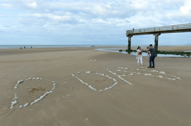 Une famille sur "Omaha Beach", où le mot "D-Day" a été tracé à l'aide de galets, à  Vierville-sur-Mer, dans le Calvados, lors des célébrations du 75e anniversaire du Débarquement en juin 2019