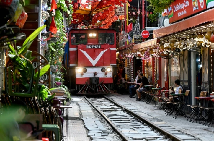 Un train passe au ras des cafés et des habitations dans la célèbre et touristique "rue du train" à Hanoi, le 18 août 2025 