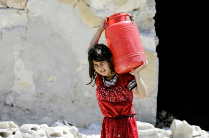 Une jeune syrienne porte un bidon d'eau dans l'ancien quartier rebelle de Kallassé à Alep, le 5 juillet 2017