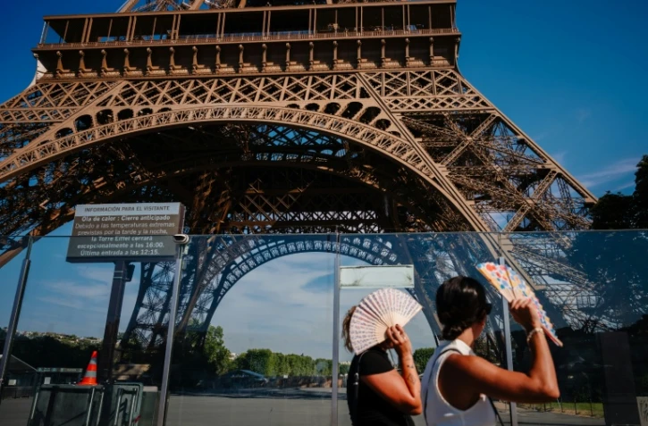 Des touristes se protègent du soleil avec des éventails en passant devant la tour Eiffel, fermée plus tôt en raison de la canicule, le 11 juillet 2026 à Paris