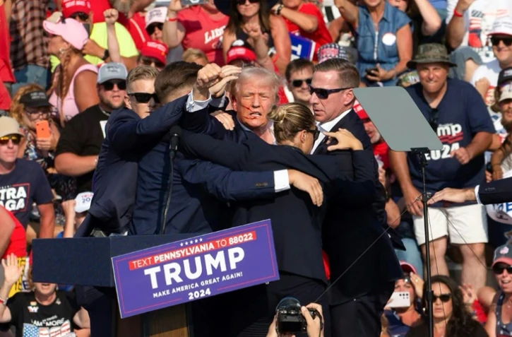 Donald Trump lève le poing en l'air au moment d'être évacué de son meeting à Butler, aux Etats-Unis, le 13 juillet 2024